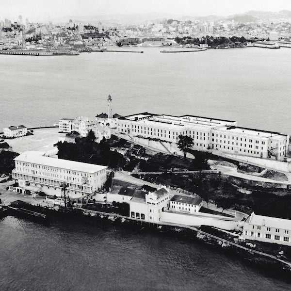 Black and white aerial view of Alcatraz Island from the mid 20th century, with San Francisco in the background