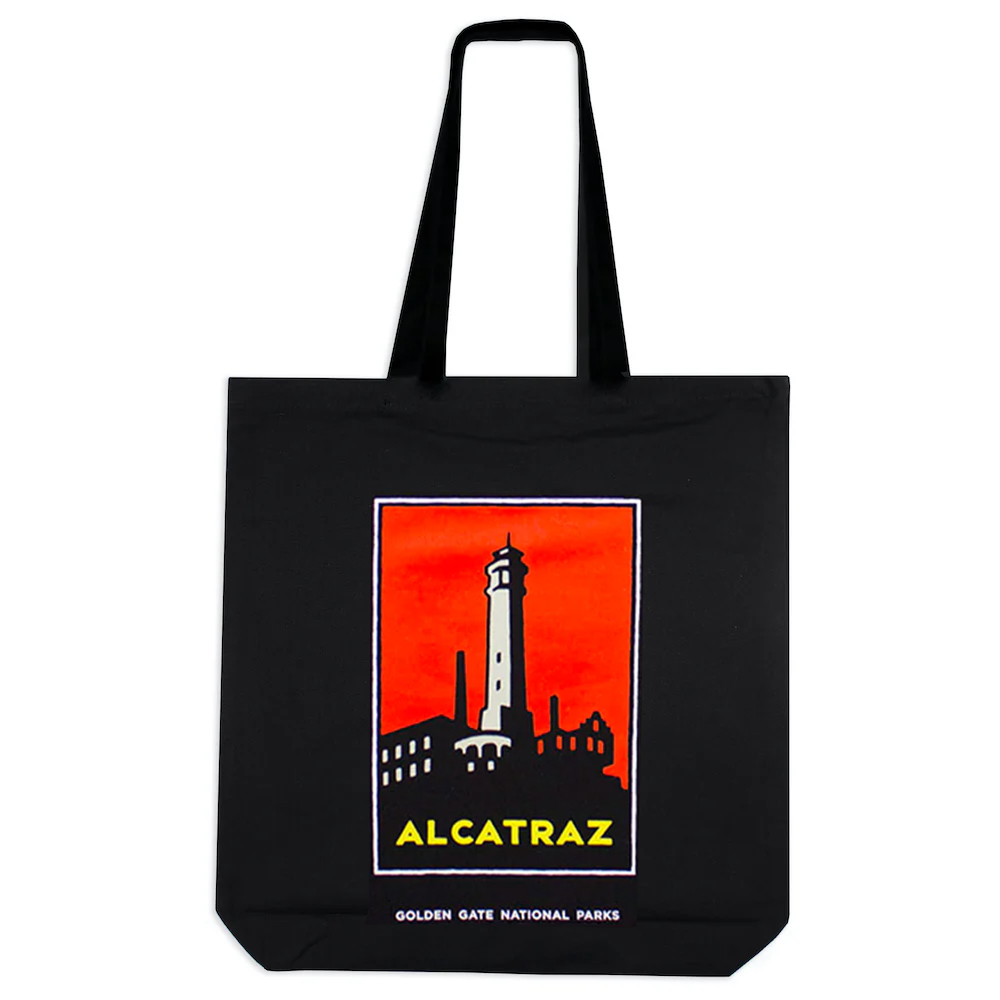 Black tote bag with colorful screen printed Alcatraz Island illustration with tree and words on front, art by Michael Schwab