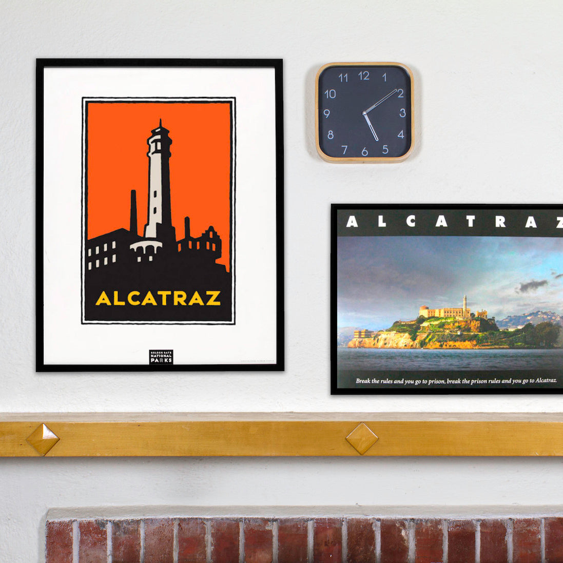 Framed Alcatraz Island posters on a white wall, with a black clock, above a wood and brick fireplace