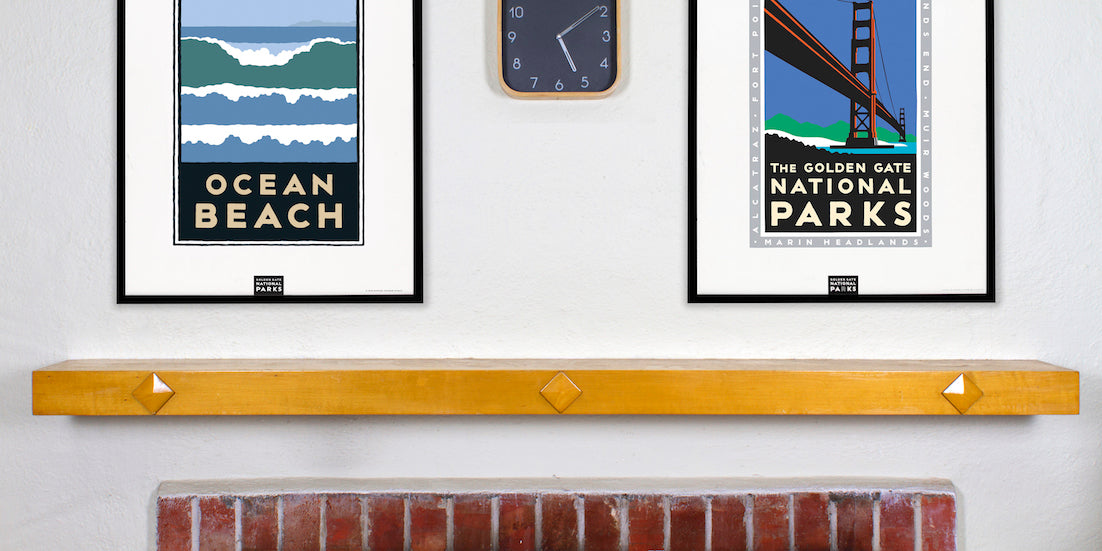 Two framed posters hang above a mantlepiece, Ocean Beach and Golden Gate National Parks.