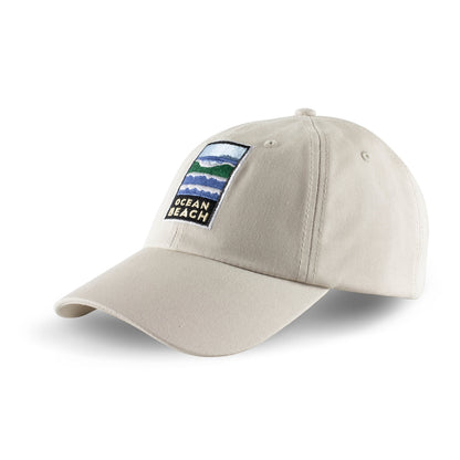 Tan baseball cap with colorful embroidered Ocean Beach logo on front panels. Artwork by Michael Schwab.
