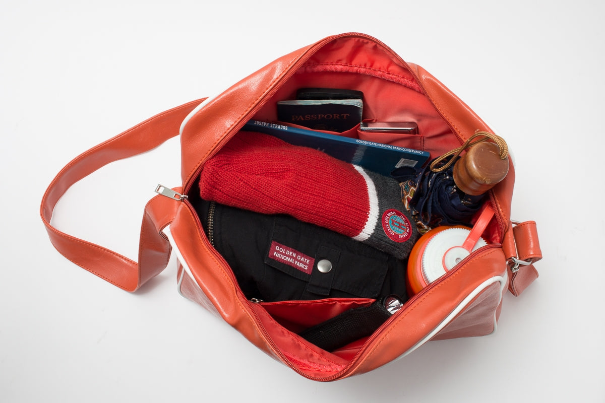 Orange carry-on bag with white trim and white design of airplane flying over the Golden Gate Bridge on front pocket.
