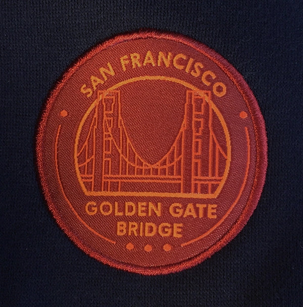 Navy blue hoodie with orange hood-lining accent and embroidered orange and red Golden Gate Bridge logo on left chest.