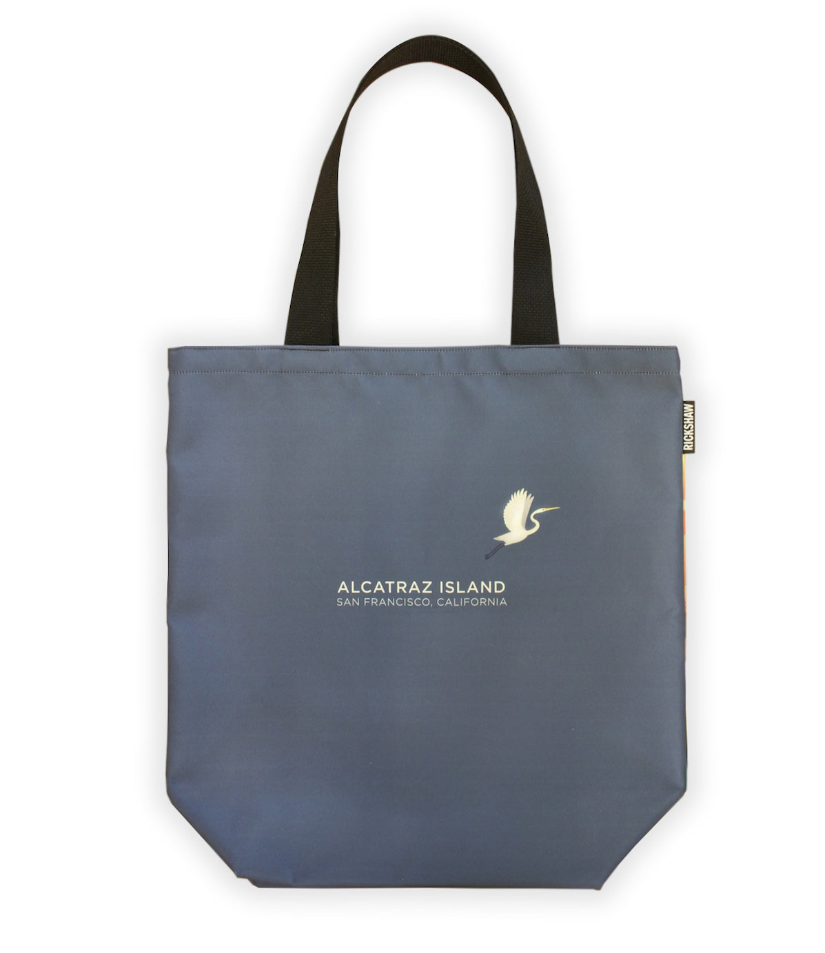 Grey-purple tote bag with white text at center “Alcatraz Island San Francisco California” and illustration of egret. Black handle.