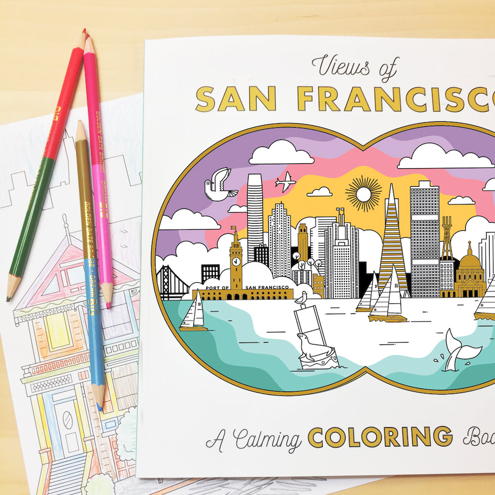 Colored pencils and “Views of San Francisco: A Calming Coloring Book” with brightly colored page sitting on a wooden table.
